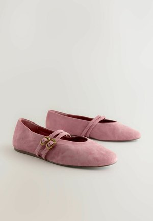 Ballerines en daim rose avec un bout pointu, dotées de deux brides décoratives avec des boucles dorées sur le cou-de-pied. Texture lisse et design minimaliste.
