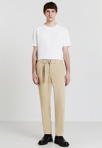 T-shirt bianco a maniche corte con texture abbinato a pantaloni beige con cintura e stivaletti neri alla caviglia. Taglio semplice e dritto, design minimalista.