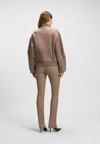 Ruskea pommittaja-takki ribatulla helmalla ja hihoilla, yhdistettynä istuviin ruskeisiin housuihin ja mustiin korkokenkiin. Sujuva pinta, minimalistinen muotoilu.