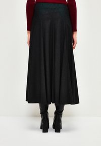 Mustaa saumattomalla midi-hameella, jossa on pystysuunnassa raidat, valmistettu teksturoidusta kankaasta, yhdistettynä polven ylle ulottuviin mustiin korollisiin saappaisiin.