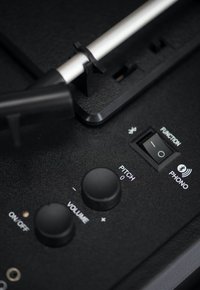 Black control panel of a device featuring knobs for volume and pitch, a function switch, and a phono input, with metallic accents.