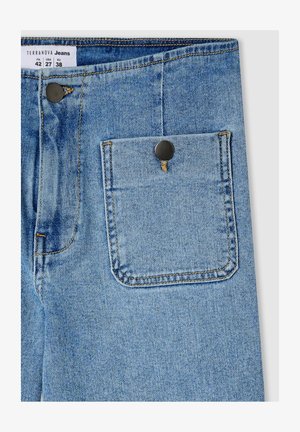 Jeans in denim azzurro chiaro con una tasca posteriore fissata da un bottone metallico nero, con dettagli di cucitura visibili e un'etichetta in tessuto in vita.