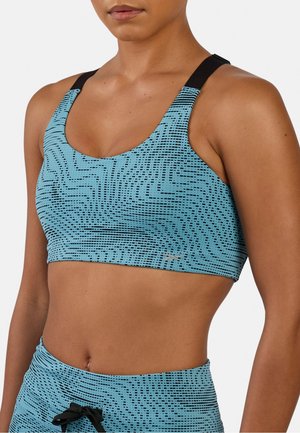 Mujer con sujetador deportivo de patrón azul y negro y pantalones cortos a juego de cintura alta con tirantes negros ajustables en los hombros.