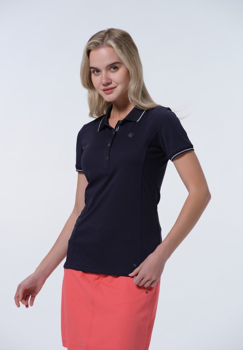 Námornícky polo tričko s bielymi detailmi, krátkymi rukávmi a zapínacím golierom. Kombinované s korálovou sukňou, která má logo na hrudi.