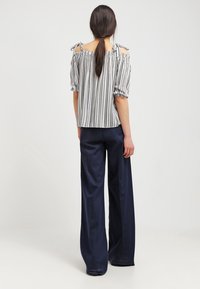 Randig off-the-shoulder topp med korta puffärmar, lätt tyg, knyts vid axlarna, kombinerad med vida marinblå byxor.