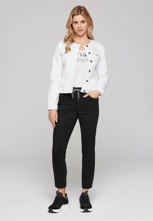 White denim jacket with button front, paired with a gray graphic t-shirt and black tapered pants. Worn with black sneakers.