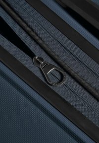 Gros plan sur une fermeture éclair en tissu bleu foncé partiellement ouverte avec des dents noires et une languette métallique argentée sur une surface texturée.