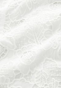 Weißer Spitzenstoff mit floralen und blättrigen Mustern, die filigrane Details und eine strukturierte Oberfläche aufweisen und ein zartes sowie elegantes Erscheinungsbild schaffen.