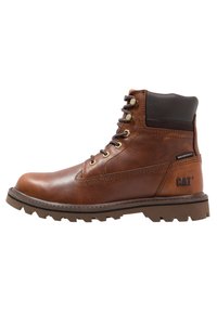 Bota de cuero marrón impermeable con punta redonda, cierre de cordones en la parte delantera, herrajes dorados, suela de goma y cuello de tobillo texturizado en marrón. Logo de CAT en el lateral.