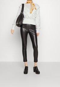 Pull tricot bleu clair avec un design à volants, associé à des leggings en similicuir noirs et des chaussures plates-formes noires sans lacets. Une écharpe rayée orange complète la tenue.