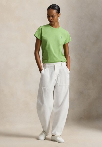 Πράσινο βαμβακερό t-shirt με κοντά μανίκια και λογότυπο στο αριστερό στήθος, συνδυασμένο με άνετο λευκό βαμβακερό παντελόνι και λευκά παπούτσια.