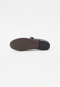 Black leather shoe sole with rounded shape, textured surface in the center, contrasting dark brown bottom, and discrete branding detail.