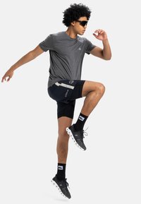 Mannen sportoutfit met een grijze T-shirt met korte mouwen, marineblauwe shorts met accentpanelen en zwarte hardloopschoenen met witte zolen.