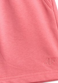 Tissu rose en gros plan avec des coutures visibles et un logo brodé "4F" près du bord inférieur.