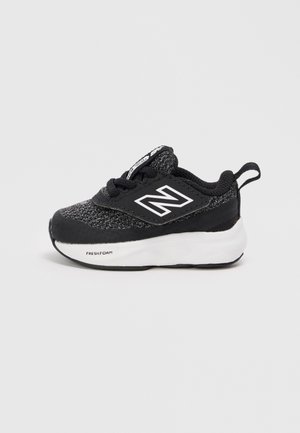 Chaussure de sport noire en textile avec un dessus en maille grise, des accents noirs et une semelle en mousse blanche. Présente un logo sur le côté.
