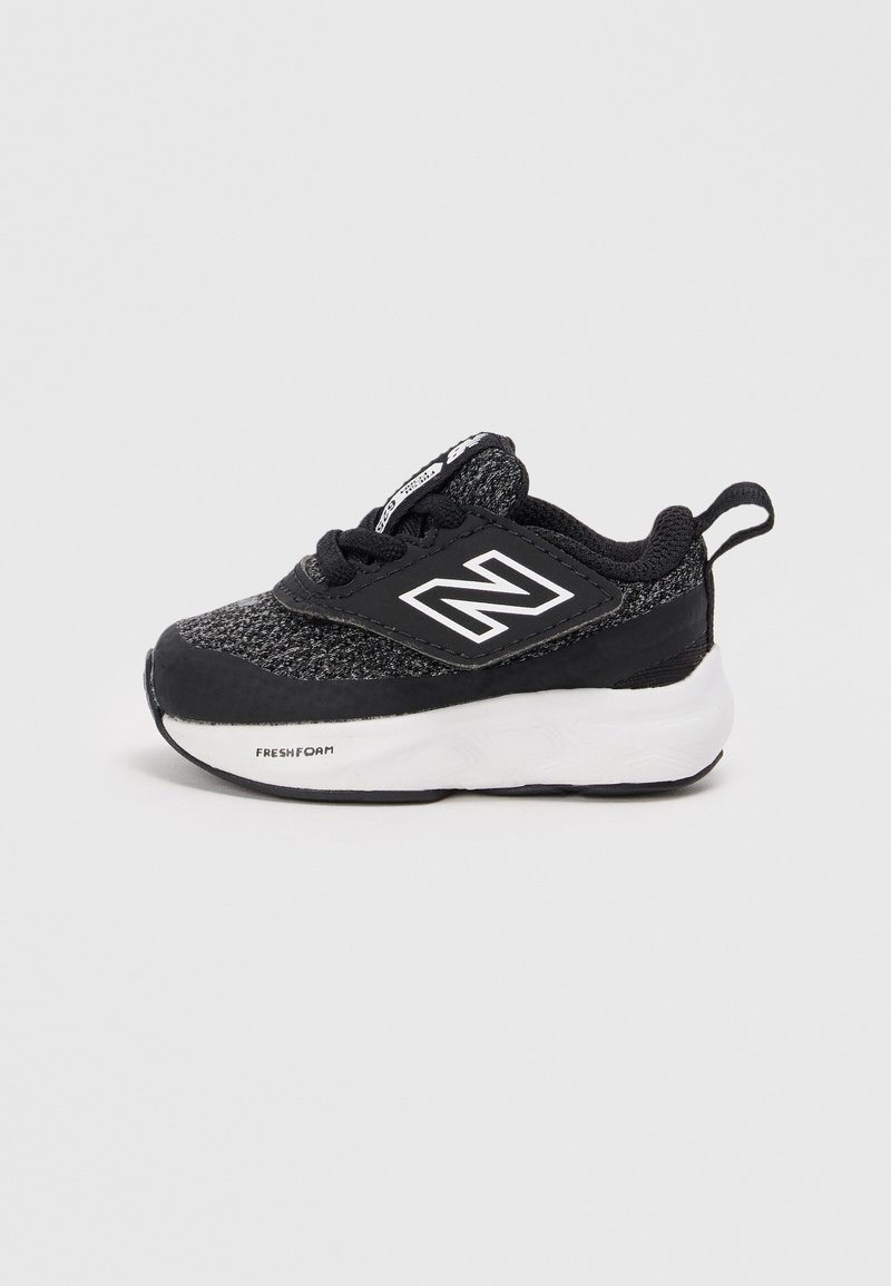Chaussure de sport noire en textile avec un dessus en maille grise, des accents noirs et une semelle en mousse blanche. Présente un logo sur le côté.