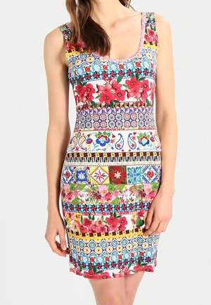 Kobieta ubrana w dopasowaną sukienkę bez rękawów z wielokolorowymi kwiatowymi i geometrycznymi wzorami ułożonymi w poziome pasy.