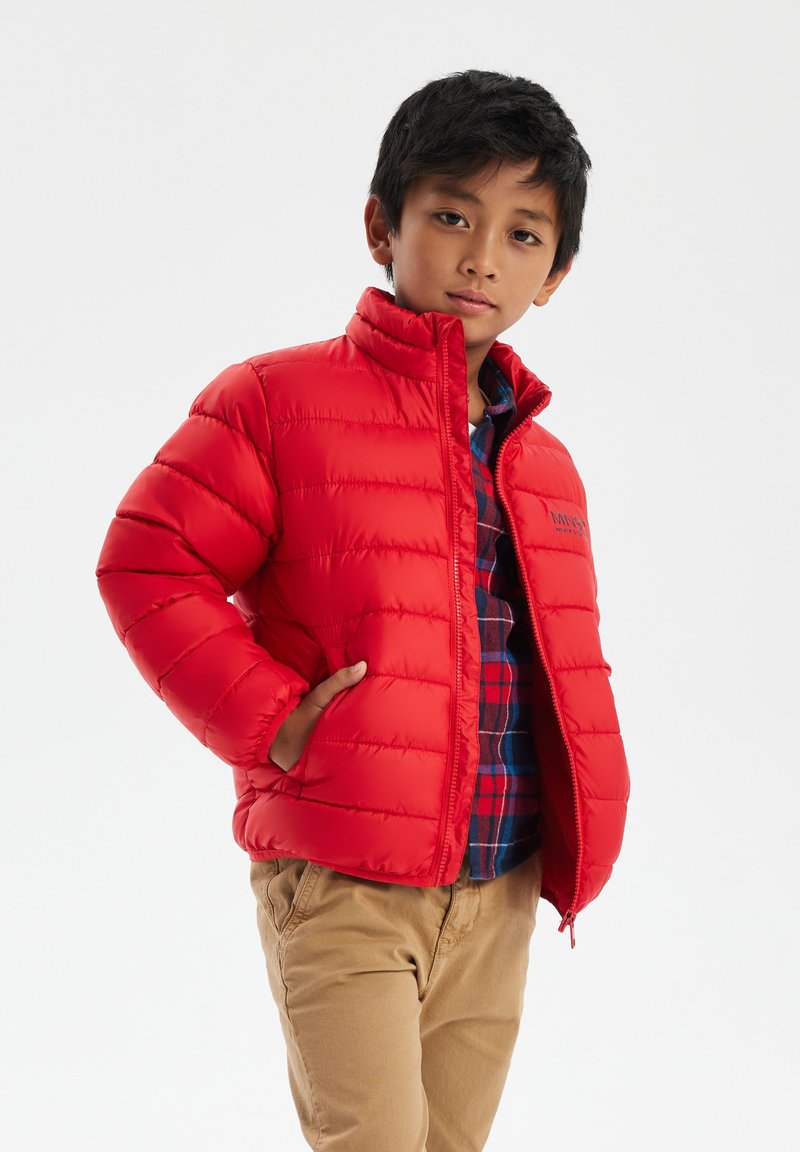 Giacca rossa in piuma con collo alto, design a righe orizzontali e tasche laterali. Indossata sopra una camicia a quadri blu e rossa.