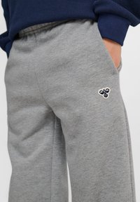 Graue Sweatpants aus weichem Stoff, mit einer lockeren Passform und einem kleinen gestickten Bienenlogo auf der linken Oberschenkeltasche.