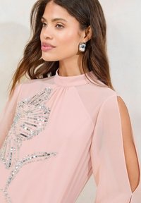 Vaaleanpunainen sifonkiblouse, jossa on läpinäkyvät hihat. Edessä on paljetein koristeltu kukkakuvaus ja avonaiset olkapäät. Suloinen ja kevyt rakenne.