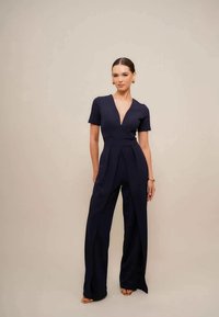 Marineblå jumpsuit med kort erm, dyp V-hals og vide ben med frontfolder. Glatt stoff med en skreddersydd passform.