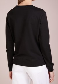 Svart sweatshirt med rund halsringning och ribbad mudd. Har en slät textur och en avslappnad passform, matchad med vita byxor.