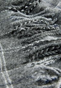 Soft gray wool fabric with fringed tassels and visible woven texture, showing close-up details of fibers and stitching.