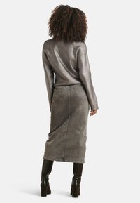 Metalen geribde lange mouw top in zilver, gecombineerd met een grijze denim midi rok met hoge taille. Zwarte kniehoge blockhakken laarzen.