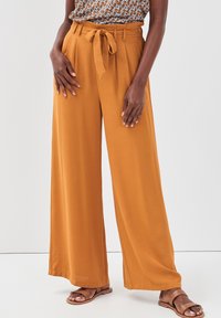 Pantalons taille haute à jambe large en orange brûlé, fabriqués à partir d'un tissu doux, avec une ceinture nouée, des plis et une texture lisse.