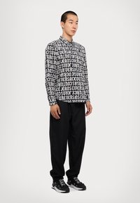 Black and white long-sleeve shirt with bold text design, paired with loose black trousers and black sneakers. Text covers the shirt evenly.