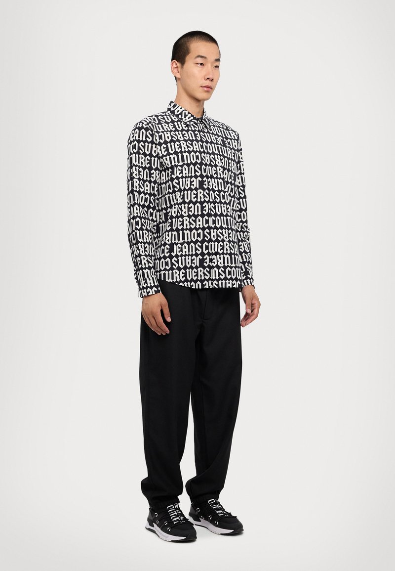 Black and white long-sleeve shirt with bold text design, paired with loose black trousers and black sneakers. Text covers the shirt evenly.