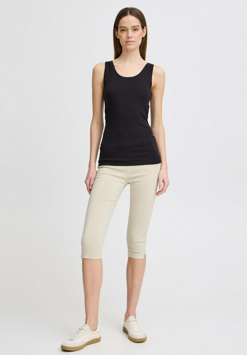 Svart ermeløs tank topp kombinert med lys beige capri leggings. Leggingsene har en tett design og blir komplementert av hvite joggesko.
