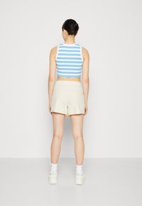 Un crop top à rayures bleues et blanches associé à un short beige clair. La tenue présente une coupe ajustée et est complétée par des baskets blanches.