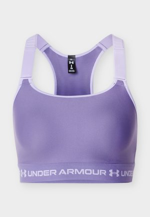Fioletowy biustonosz sportowy Under Armour z szerokimi regulowanymi ramiączkami i elastyczną taśmą z logo na dole.
