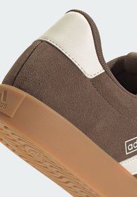 Smeđi nubuk tenisice s bijelim kožnim detaljima, koje imaju teksturiranu gumenu potplatu i logo detalj sa strane.