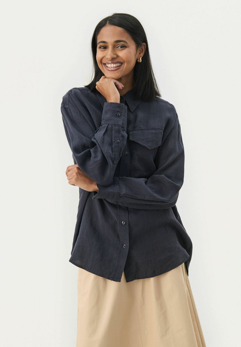 Donker marineblauwe button-up shirt met lange mouwen, een enkele borstzak, een zachte textuur en een rechte zoom, gecombineerd met een lichtbeige rok.