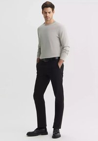 Jasnoszara koszula z długim rękawem, czarne spodnie i czarne buty. Koszula ma okrągły dekolt; spodnie są proste. Ogólnie prosty design.