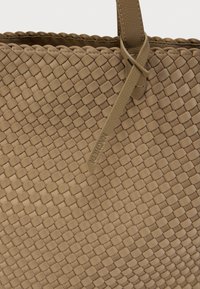 Μπεζ υφαντή δερμάτινη τσάντα tote με υφή και σχέδιο crosshatch, με ανθεκτικές λαβές και διακριτική εμβληματική ετικέτα με ανάγλυφο λογότυπο.