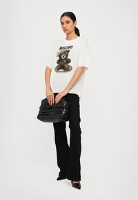 Maglietta bianca oversize con grafica di un orso, abbinata a pantaloni neri svasati e una borsa nera strutturata. Scarpe nere lucide completano l'outfit.