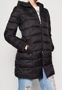 Černá zimní bunda s kapucí, se zipem vpředu, rozdělená na prošívané sekce a bočními kapsami se zacvakávacími uzávěry.