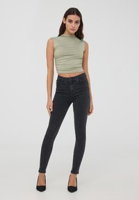 Top senza maniche verde chiaro con un design arricciato, abbinato a jeans skinny neri a vita alta con sottili decorazioni e tessuto testurizzato.