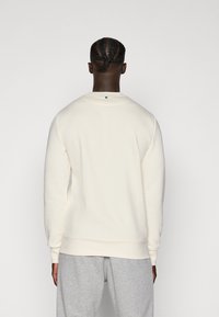 Cremfarbener Sweatshirt mit Rundhalsausschnitt und langen Ärmeln, ausgestattet mit einem gerippten Saum und Bündchen. Glatte Textur, minimalistisches Design.