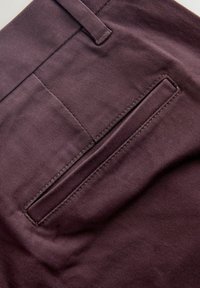 Bordowy materiał o gładkiej fakturze, z jedną tylną kieszenią o poziomym otwarciu i starannie wykonaną nicią.