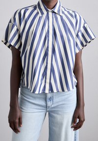 Blue and cream horizontal striped short-sleeve shirt with a pointed collar and loose-fitting design; made of lightweight fabric.