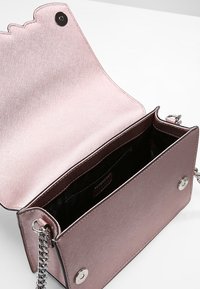 Vaaleanpunainen metallinhohtoinen olkalaukku, jossa on teksturoidu pinta, hopeiset metalliosat ja nepparikiinnitys. Sisäpuolella musta vuori ja tasku.