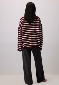 Maglione oversize a righe marrone e bianco con spalle cadute, abbinato a pantaloni neri a gamba larga. Texture in maglia morbida, vestibilità comoda.