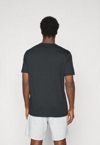 Schwarzes T-Shirt mit kurzen Ärmeln und rundem Halsausschnitt, aus Baumwolle gefertigt, mit einer glatten Textur und einem schlichten Design. Trägt helle graue Shorts.