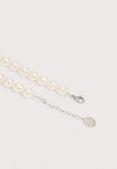 Valge ümmarguste helmestega pärliga kaelakee, millel on hõbedane homaarlukuga kinnis ja reguleeritav kett, mis lõpeb väikese ovaalse metallist sildiga.