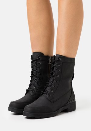 Bottes noires à lacets jusqu'à la cheville avec une finition en cuir lisse, œillets métalliques, fermeture éclair latérale et semelle texturée. Bout renforcé et accents au talon.