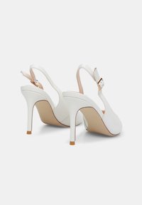 Bele slingback pete z visokim štiletom, iz gladkega usnja, z nastavljivim gležnjevim trakom in subtilnimi svetlo rjavimi detajli na podplatu.